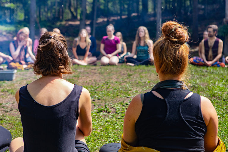 Diverse people enjoy spiritual gathering A closeup and rear view of two women, sitting around a campfire with like minded people in deep meditation during a nutrition wellness retreat in nature.