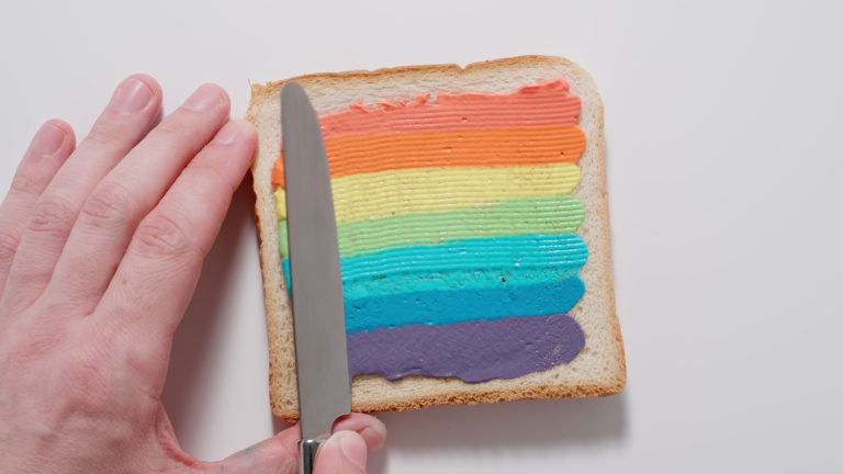 LGBTQIA+ Affirming Care. Rainbow. Male spreading colorful paste on a toast with knife.