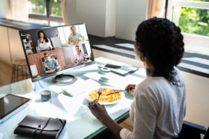 Woman eats lunch during a virtual meeting on her computer