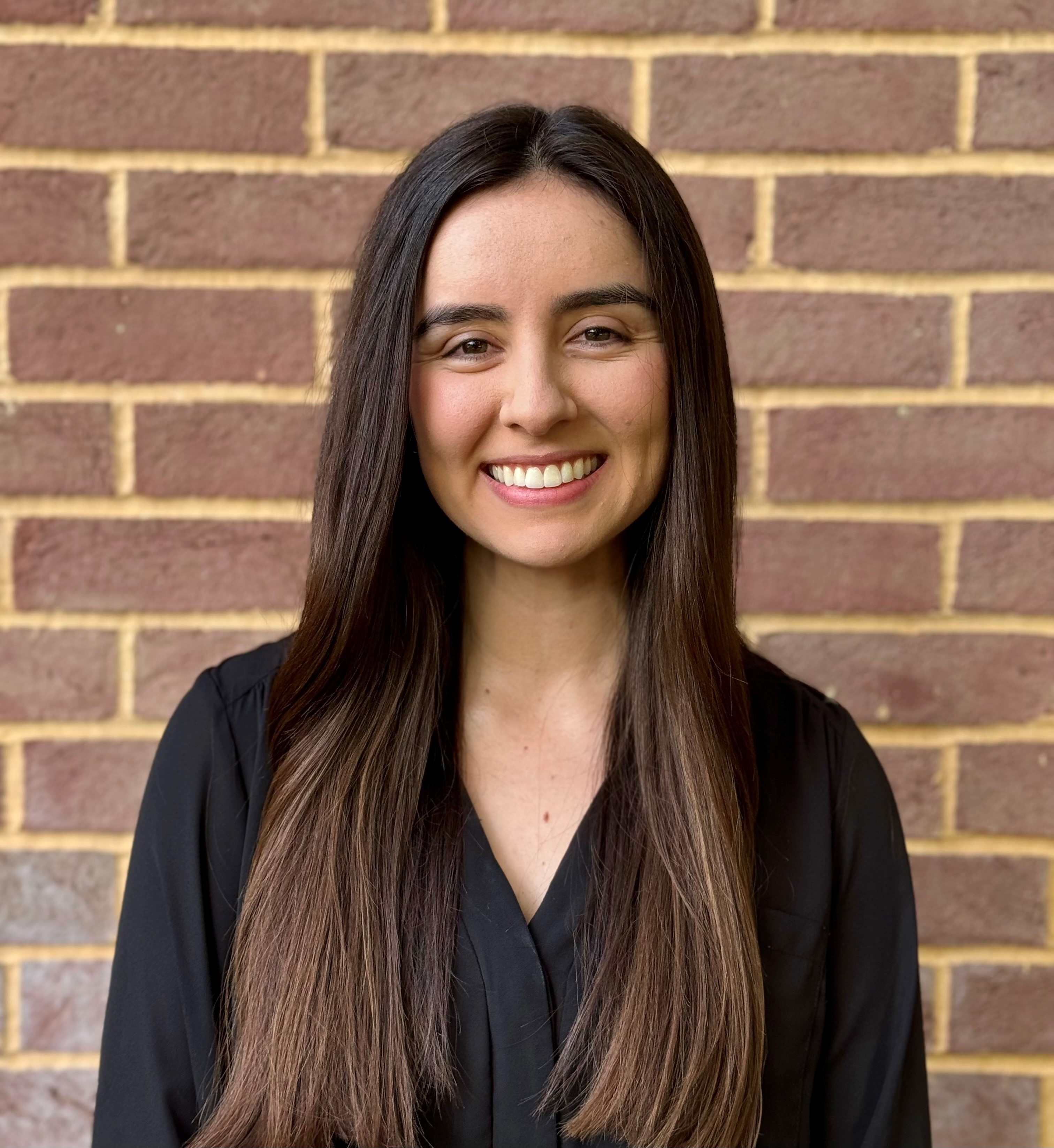 Alejandra Amezola-Velazquez smiling in front of a brick wall