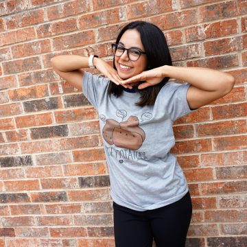 a woman wearing a t-shirt with a potato on it is standing in front of a brick wall